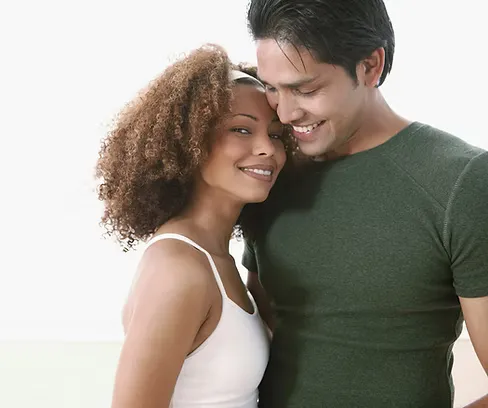 A smiling interracial couple embracing in a bright room.