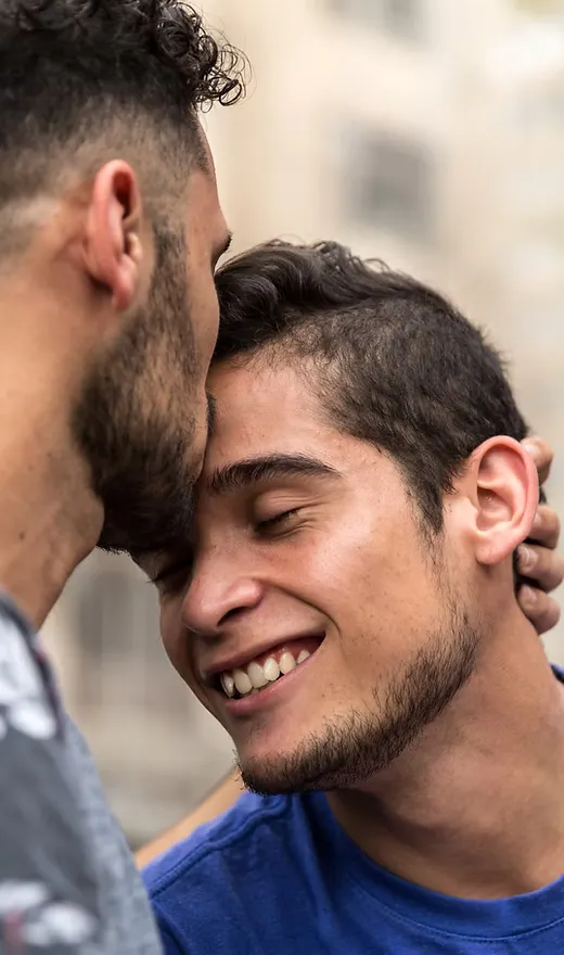 A man kissing his male partner on the forehead.